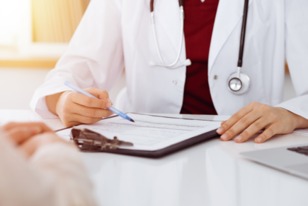 médecin en blouse blanche écrivant sur une feuille de soins à la fin d'une consultation