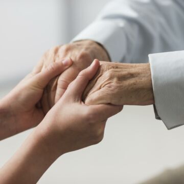 Personne jeune tenant les mains d'une personne âgée qui souffre de la maladie de Charcot. Freepik