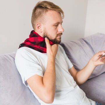 Jeune homme avec une écharpe autour du cou souffrant d'une angine blanche avec maux de gorge, fièvre et fatigue. Freepik
