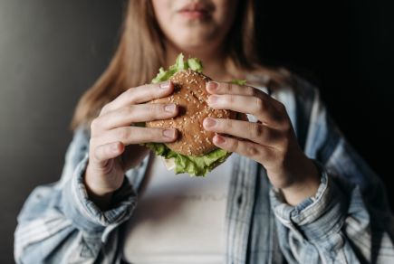 Jeune femme souffrant d'hyperphagie boulimique qui mange un hamburger alors qu'elle n'a pas faim.
