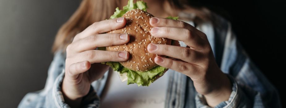 Jeune femme souffrant d'hyperphagie boulimique qui mange un hamburger alors qu'elle n'a pas faim.