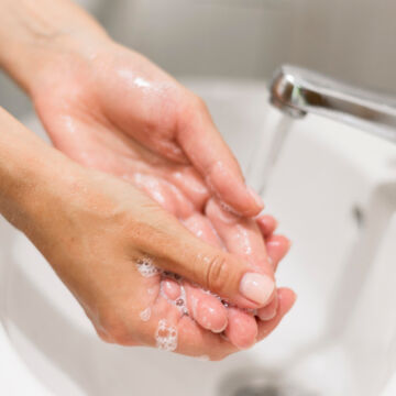 Personne qui se lave les mains dans un lavabo pour respecter les gestes barrières et éviter une angine. Freepik