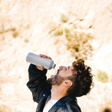 Homme qui boit de l'eau à sa gourde au soleil. Freepik