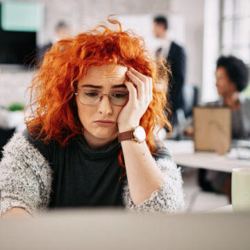 Jeune femme rousse épuisée devant son ordinateur.