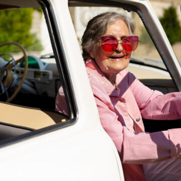 Femme âgée qui participe à l'atelier de prévention le bon temps au volant. Installée dans sa voiture elle porte des lunettes de soleil roses.