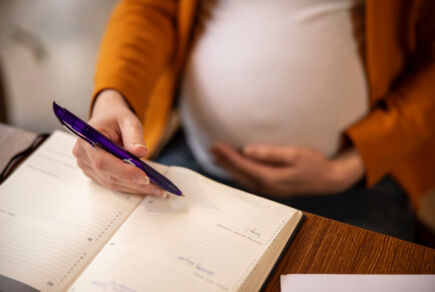 Femme enceinte après une procréation médicalement assistée qui note ses rendez-vous médicaux dans son agenda.